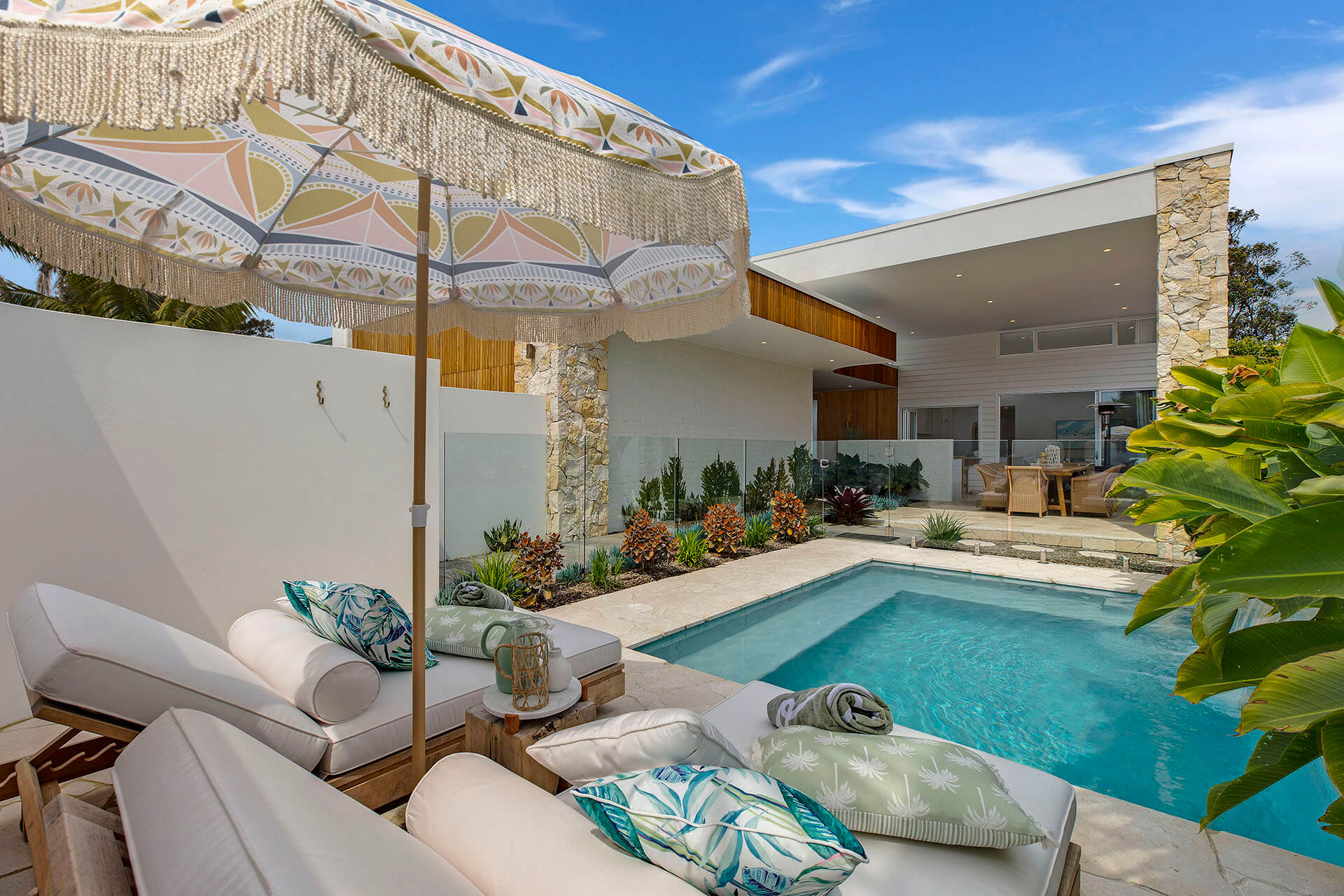Pool area with beach chairs and gardens next to modern house