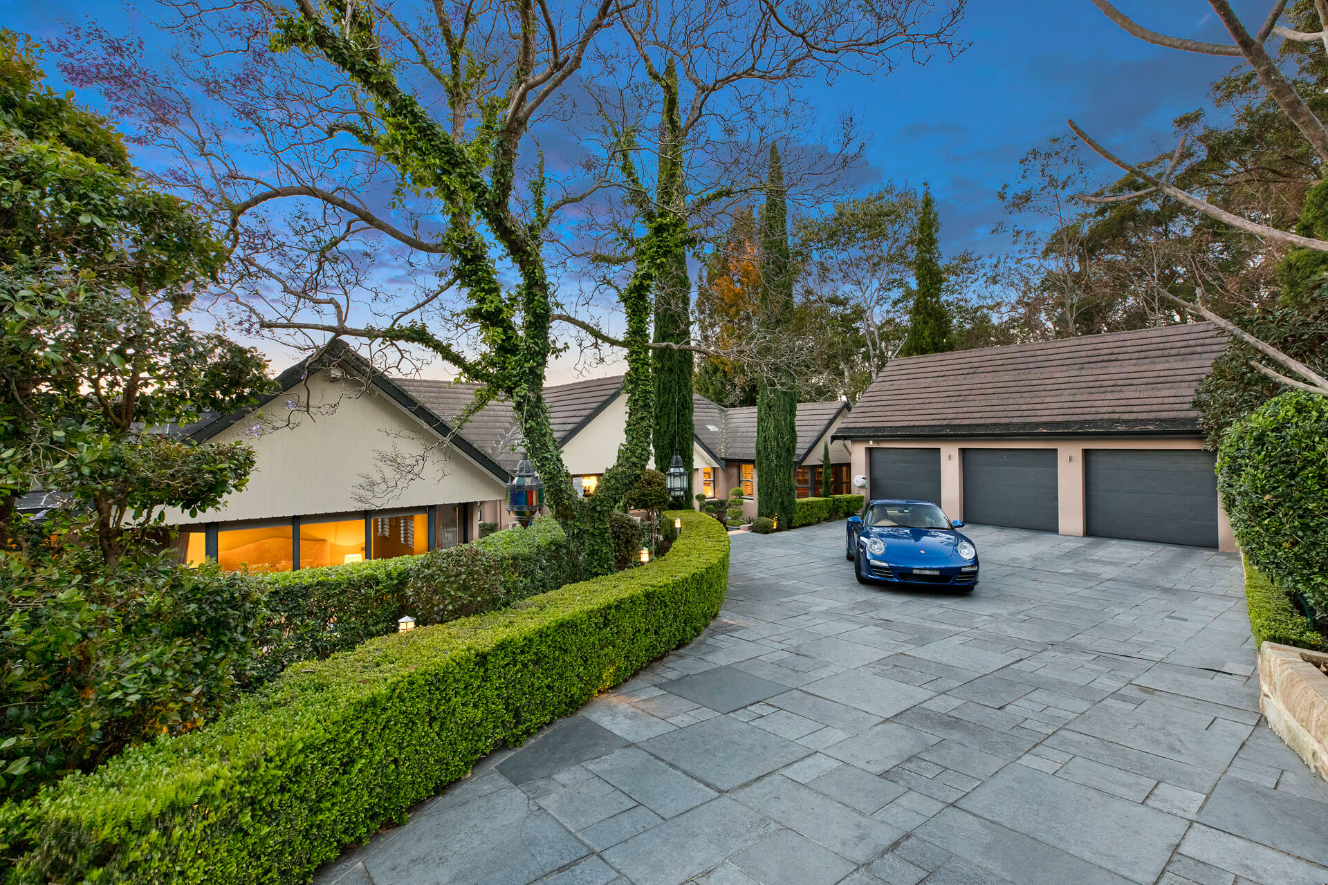 Front of modern home and garage with hedges and blue car on driveway
