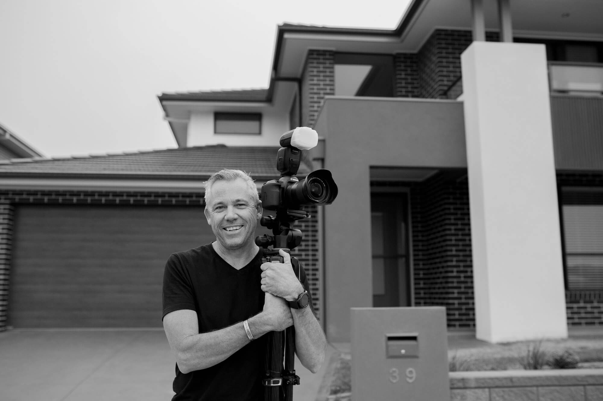 Toby holding a camera in front of a modern house
